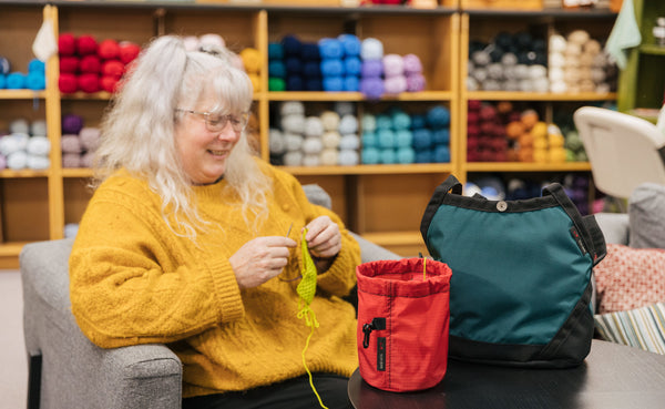 A person knitting out of a Yarn Stuff Sack with a full Little Swift beside it.